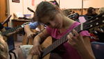 A student plays guitar along with her teacher and the rest of the class.