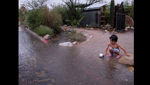A child plays in the rain near a freshly filled rain water basin.