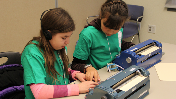 Beatrise Silva (left) and Evamaria Tanori Contreras, both 11, practice on a Victor Reader Stream device before taking the speed and accuracy portion of the Braille Challenge.