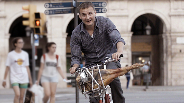 Host Phil Rosenthal bikes through streets of Barcelona with a leg of world-famous jamon.