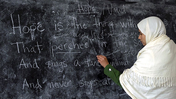 Yalda writes Emly Dickinson's "Hope is the Thing with Feathers" poem on the blackboard.