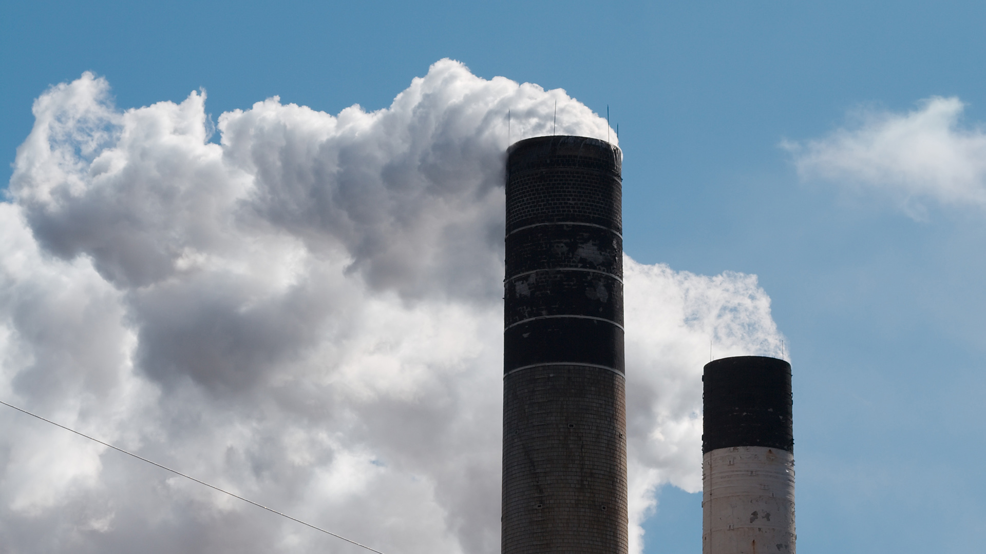 Smokestacks emit smoke into a blue sky.