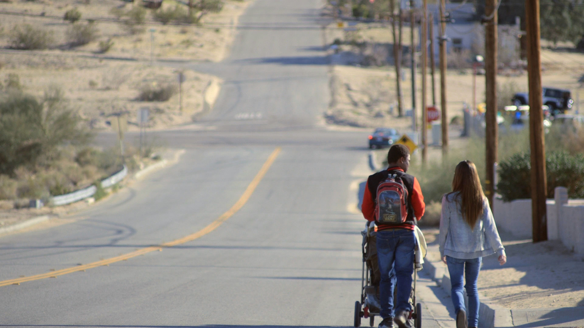 Students Lee Bridges and Layla Schneider walk with their baby towards a bus stop in Twentynine Palms, CA.
