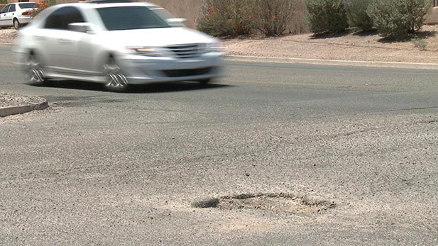 A car travels near potholes on a Tucson-area street.