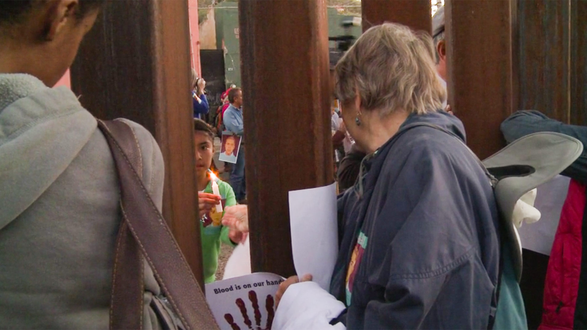 A woman passes a candle from Nogales, Arizona, through the border fence to a child at an April 2013 protest over the death of Jose Antonio Elena Rodriguez.