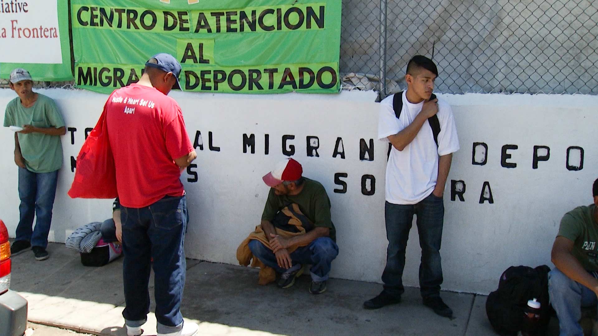 Men stand outside the Kino Border Initiative, which bears signs in Spanish signaling services for deported immigrants in Nogales, Sonora (2017).