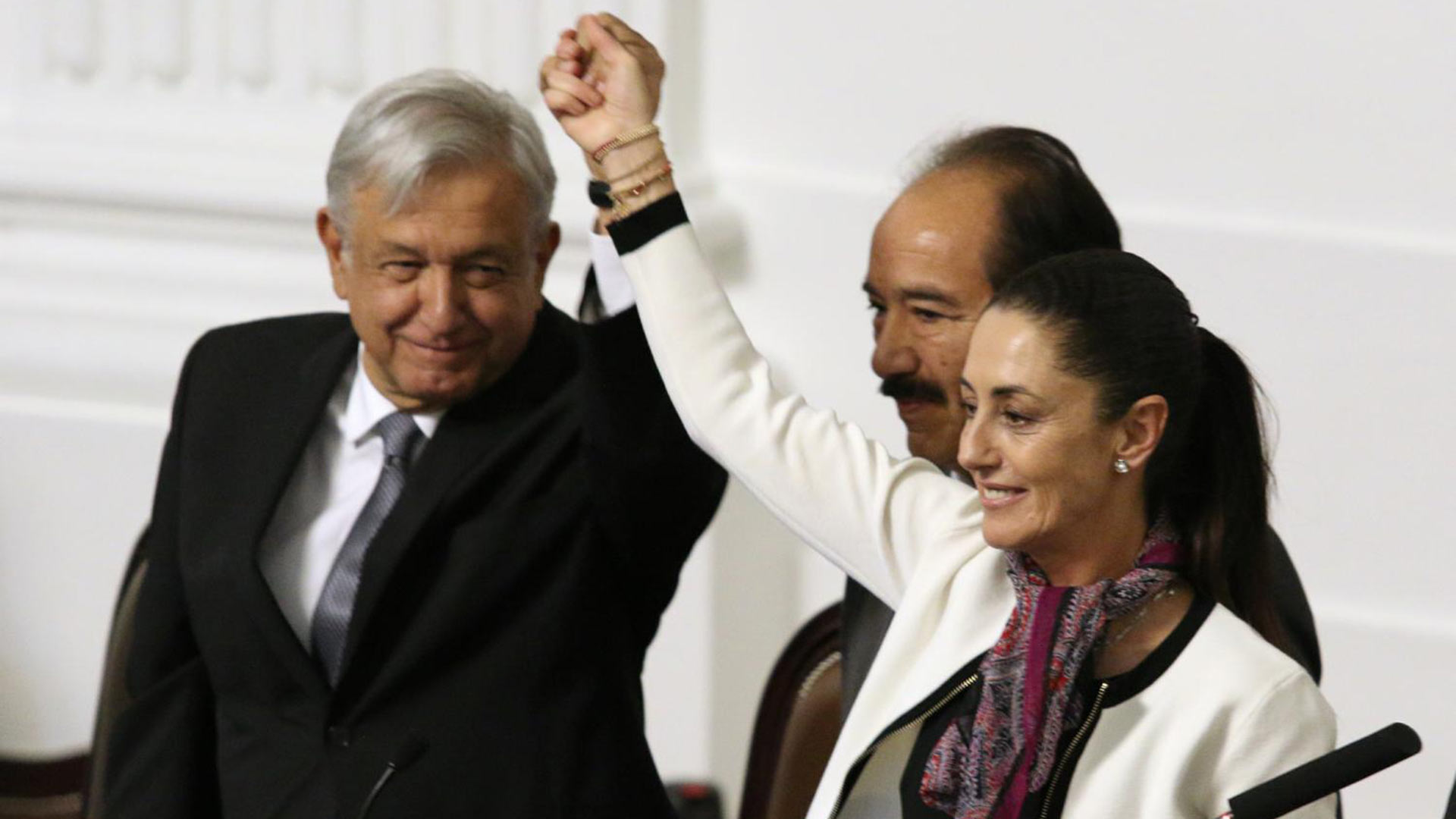 Claudia Sheinbaum Pardo, Mexico City’s first elected female mayor, holds up a hand with President Andrés Manuel López Obrador as Mexico City Congress President José de Jesús Martín del Campo looks on.