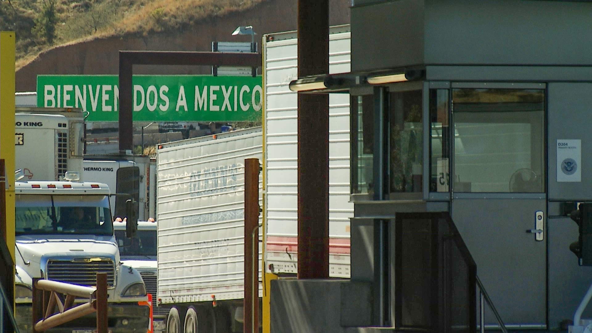 Trucks wait in line to cross into the United States via Nogales, while a sign reading "Bienvenidos a México" welcomes those crossing into Mexico.