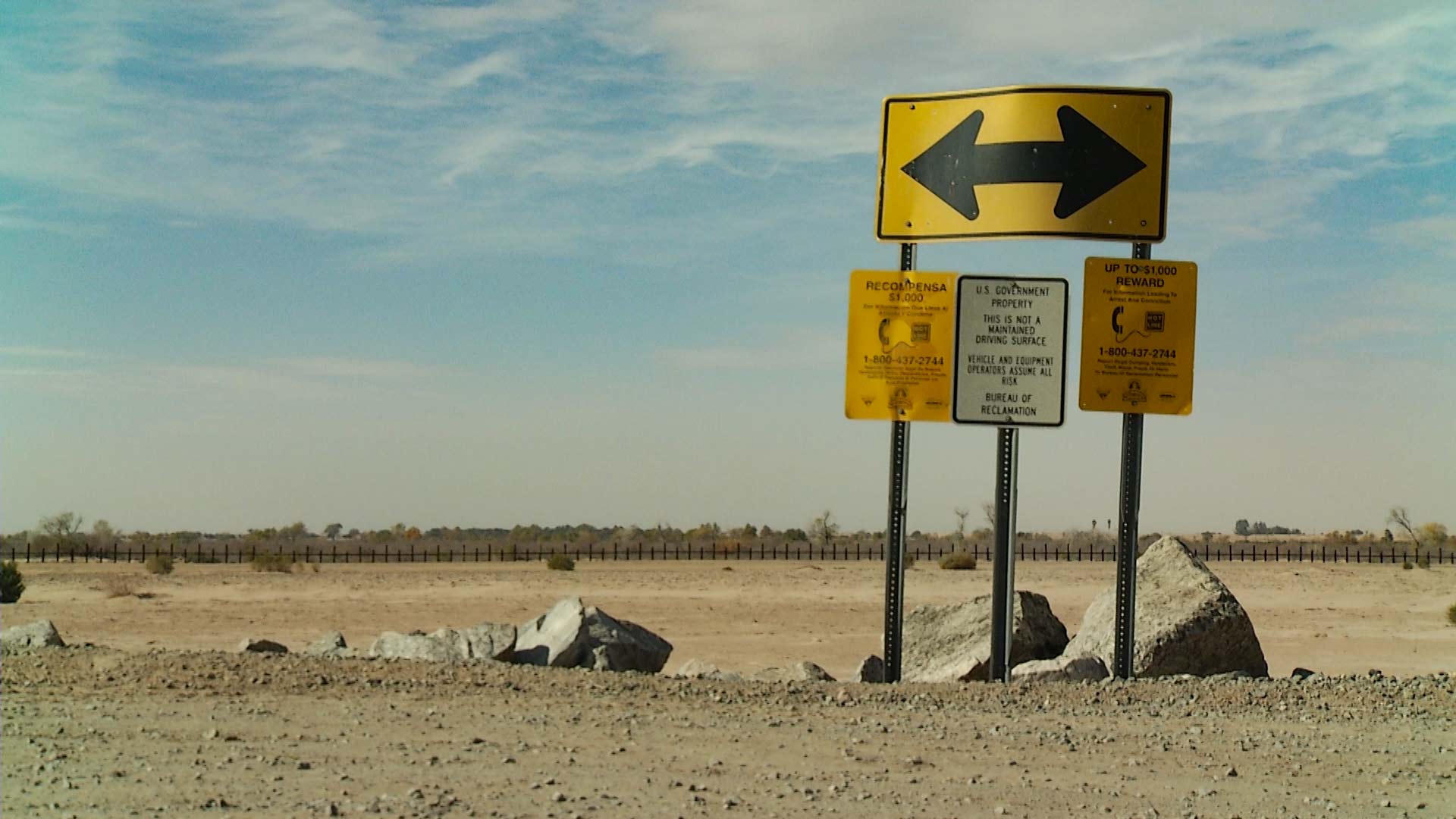 Signs posted in the Yuma Sector. In the background, a border vehicle barrier can be seen.