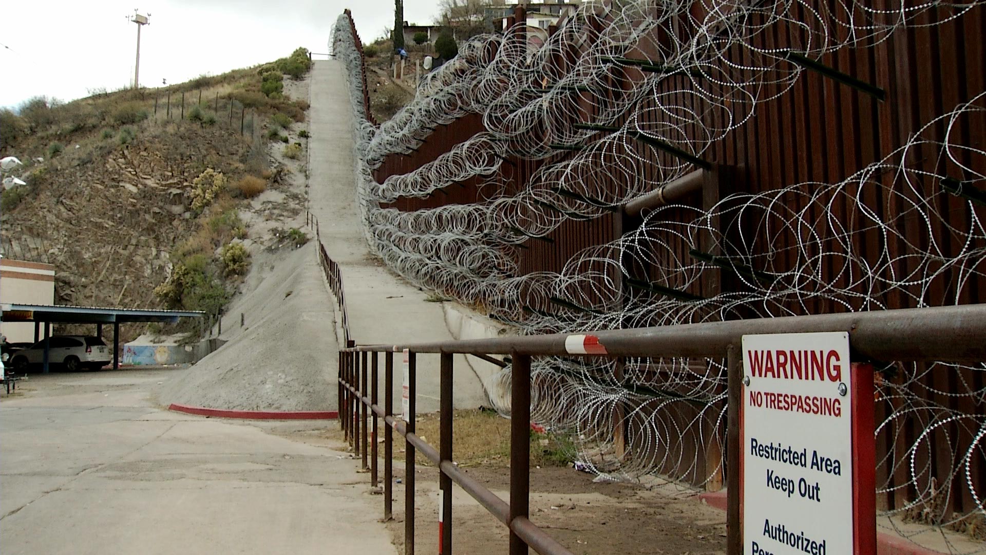 A sign warns against trespassing on federal property in front of bollard fencing covered in concertina wire at the international border in Nogales, Arizona. 