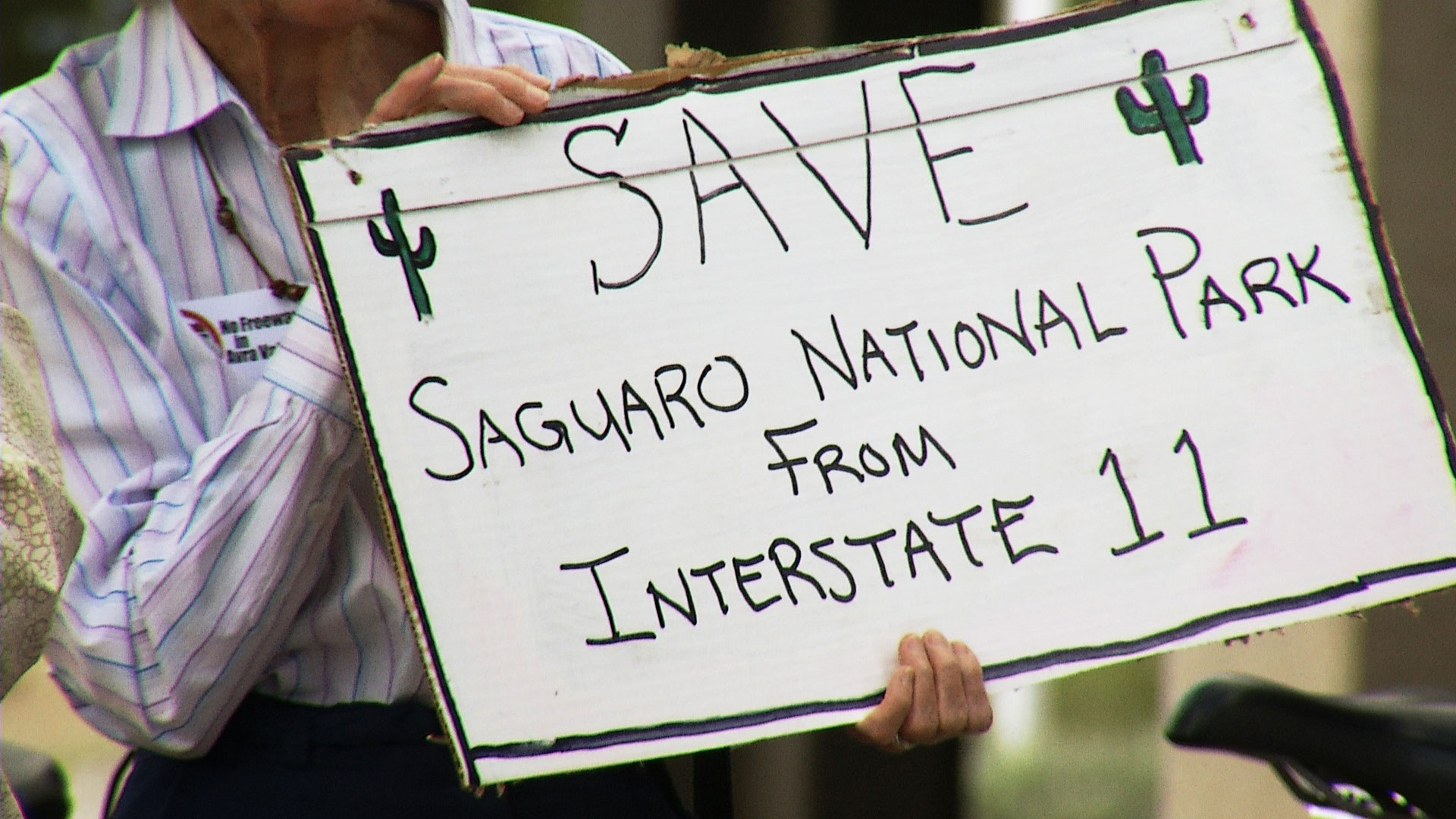 A woman holds a sign opposing early plans for a proposed Interstate 11 outside a public event focused on the corridor in Tucson on May 8, 2019. 