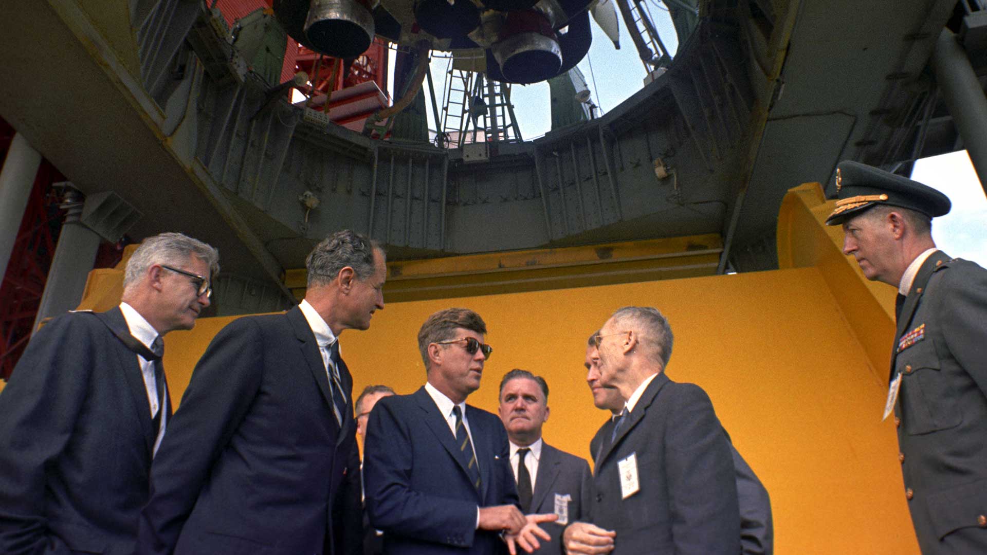 President John F. Kennedy (with sunglasses) is briefed by NASA officials at the Saturn rocket at Pad B, Complex 37, Cape Canaveral, Florida.