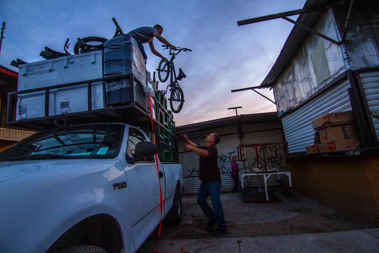 His teenage son, Emilio, hands him a bicycle from the top of a recent load of used Arizona goods that he brought back to the Hector Espino Tianguis.