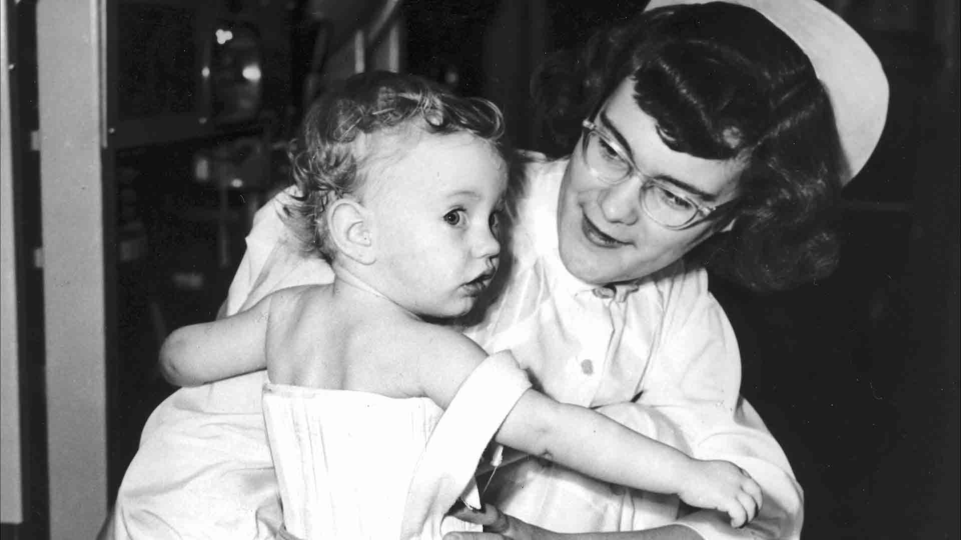 Nurse holds toddler, who is wearing leg and chest braces.