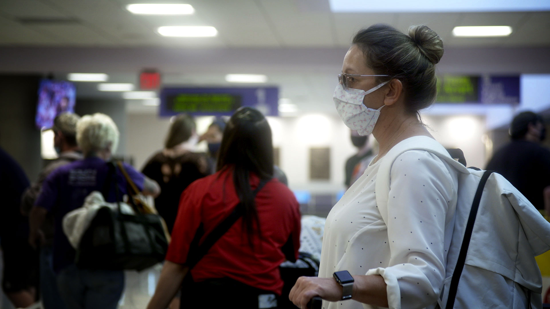 A woman stands with her luggage in the baggage claim area of the Tucson International Airport on August 10, 2020. 