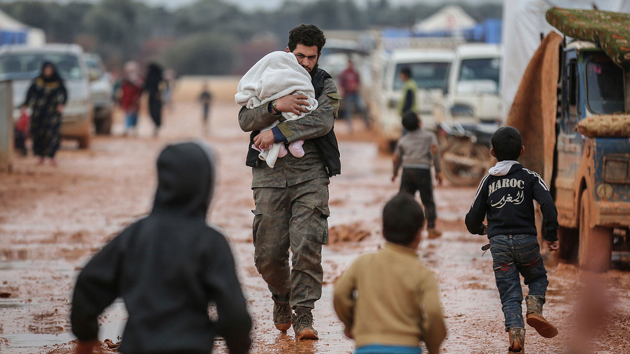 A Syrian man carries his baby at a makeshift camp for families displaced from Idlib countryside as a result of the bombing and military operations on Feb. 18, 2020.

