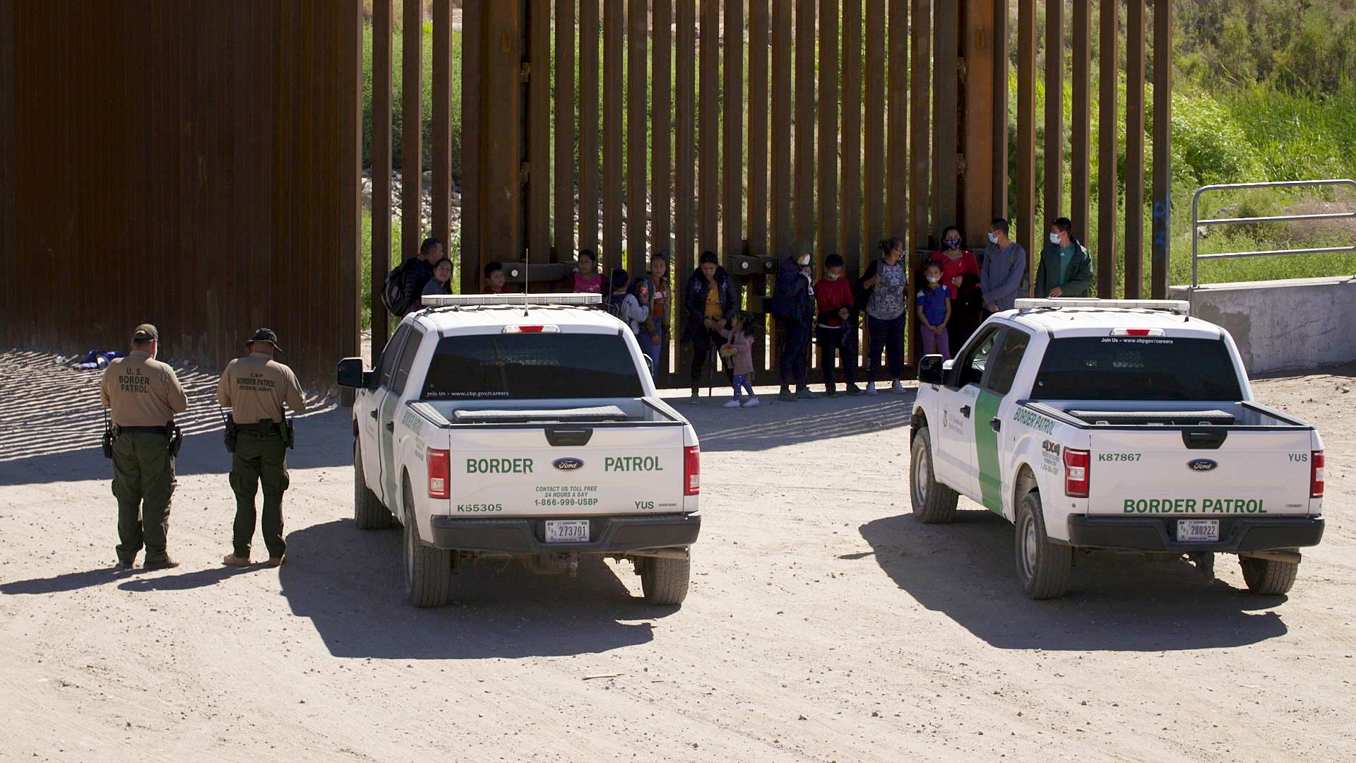 A group of migrants and Border Patrol agents along the border fence in Yuma County. June 2021. 