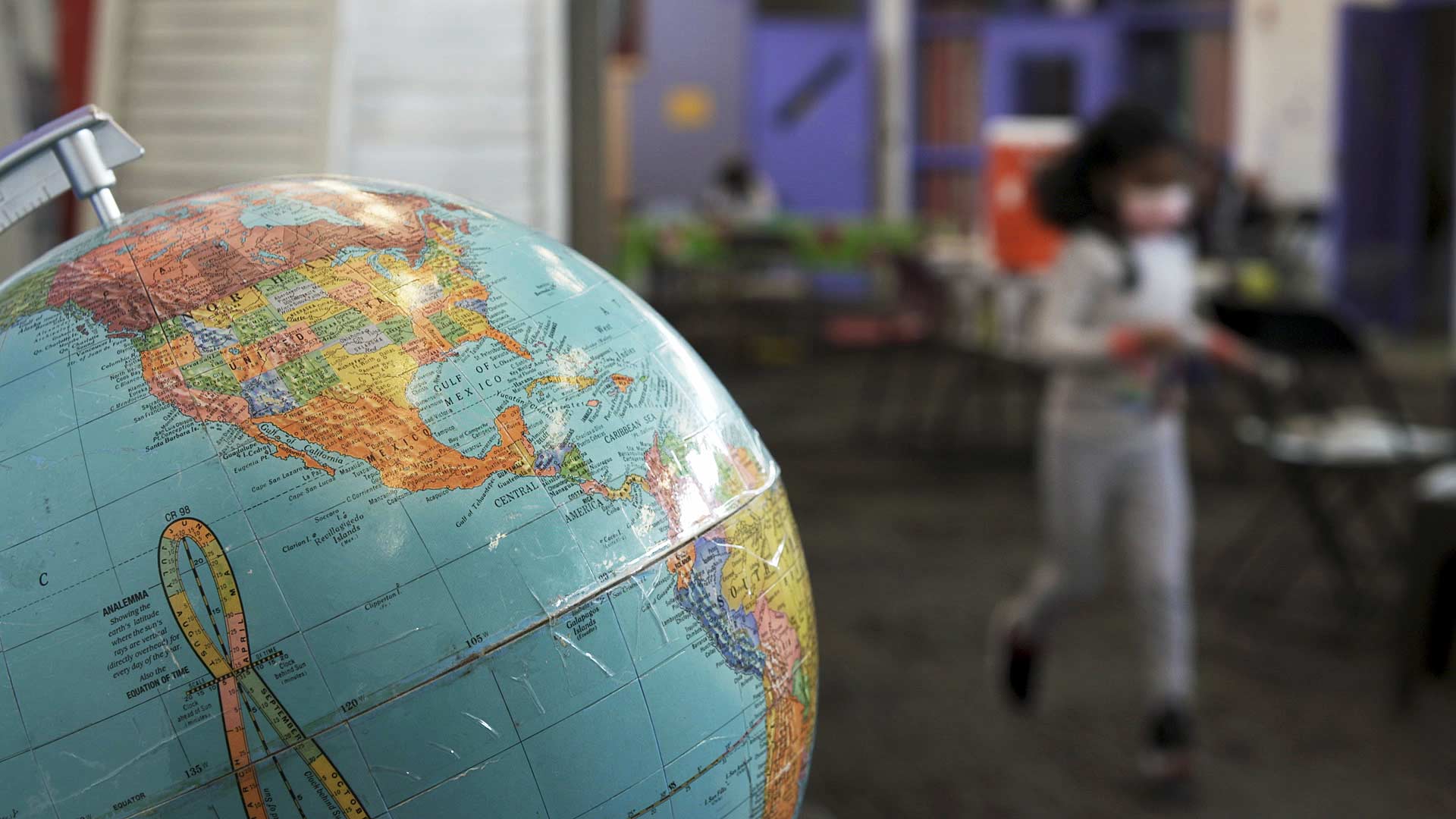 A globe is visible in the foreground as a child runs past at Casa Alitas in Tucson. The nonprofit offers shelter, medical aid and helps arrange travel for migrants admitted into the United States. 