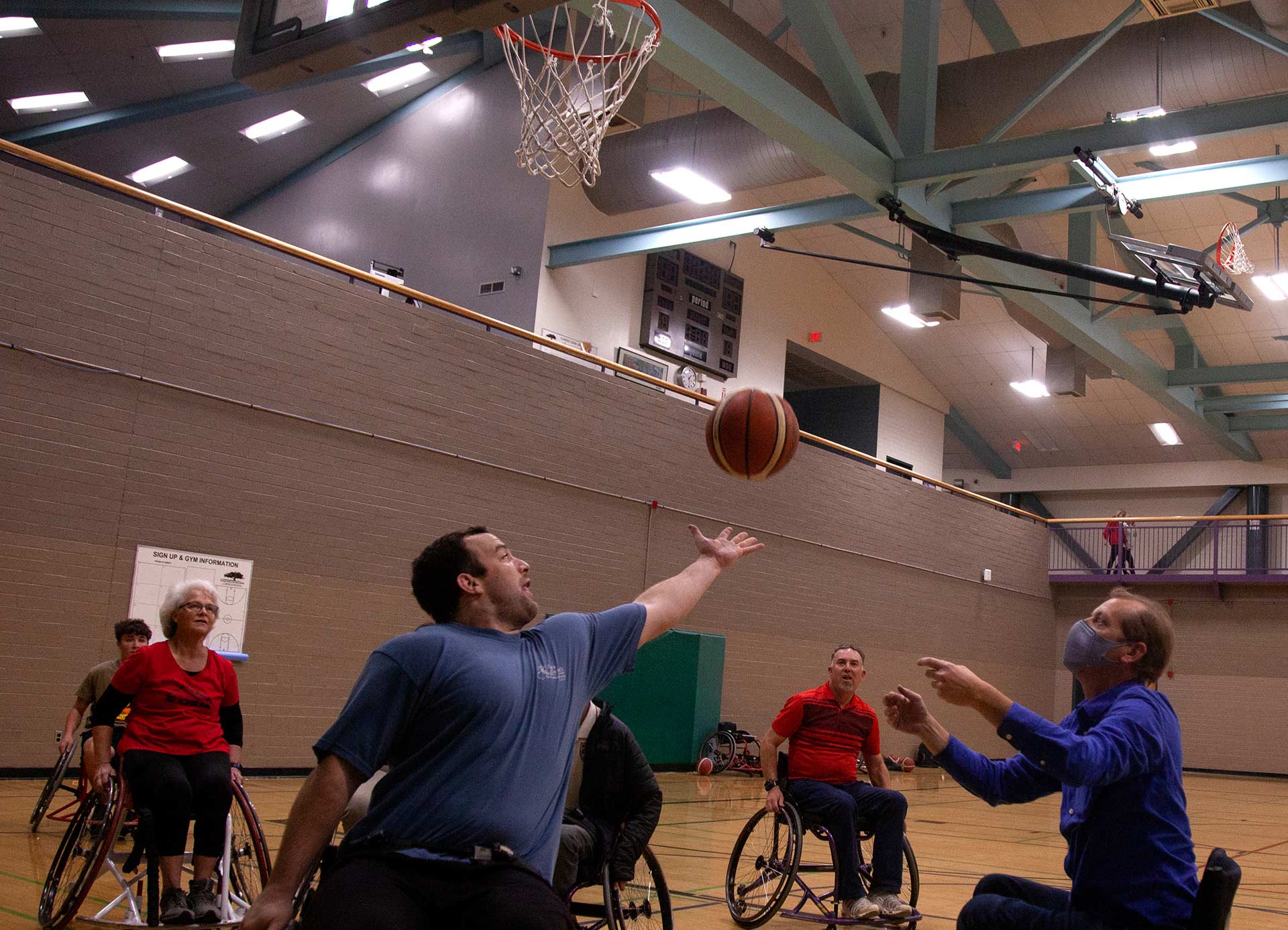 A basketball is mid-air as a group of people playing wheelchair basketball try to catch it. 