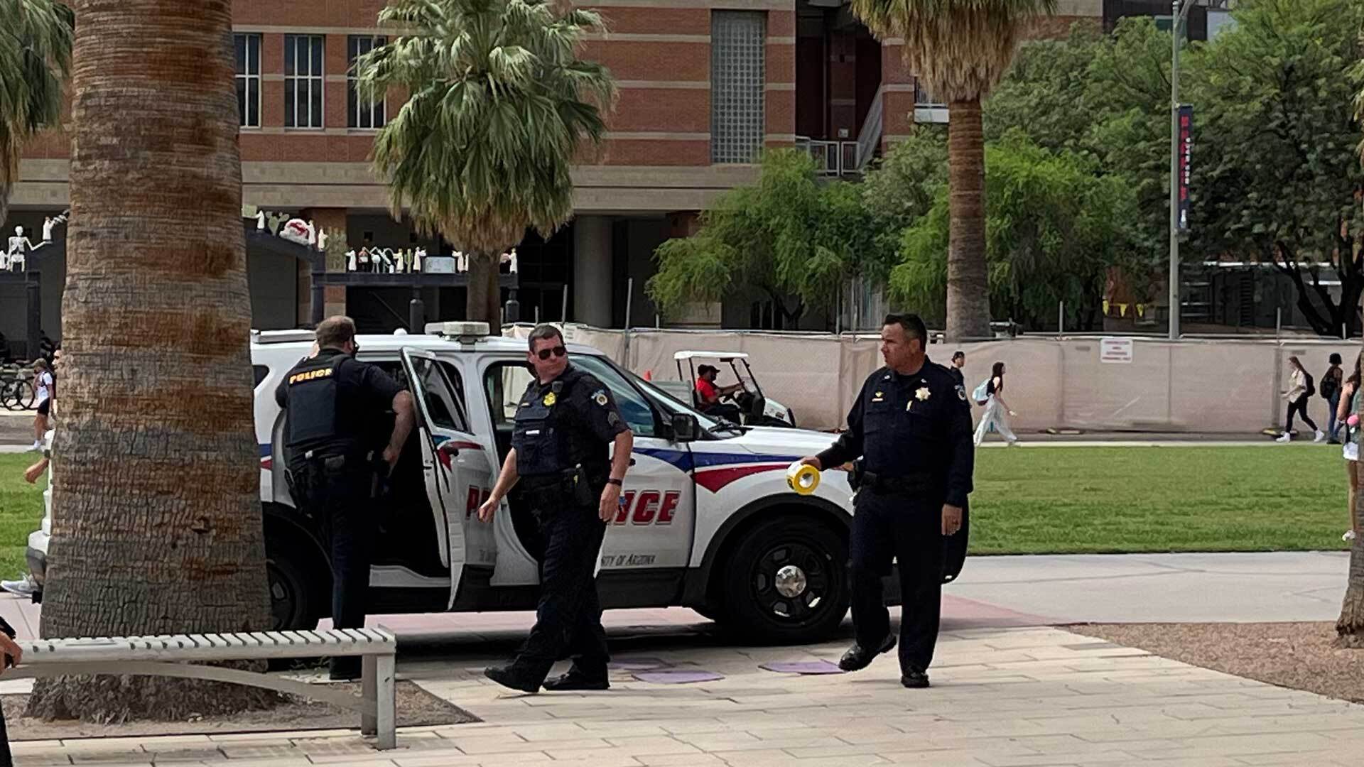 An armed suspect sits in the back of a UAPD patrol vehicle, surrounded by officers.