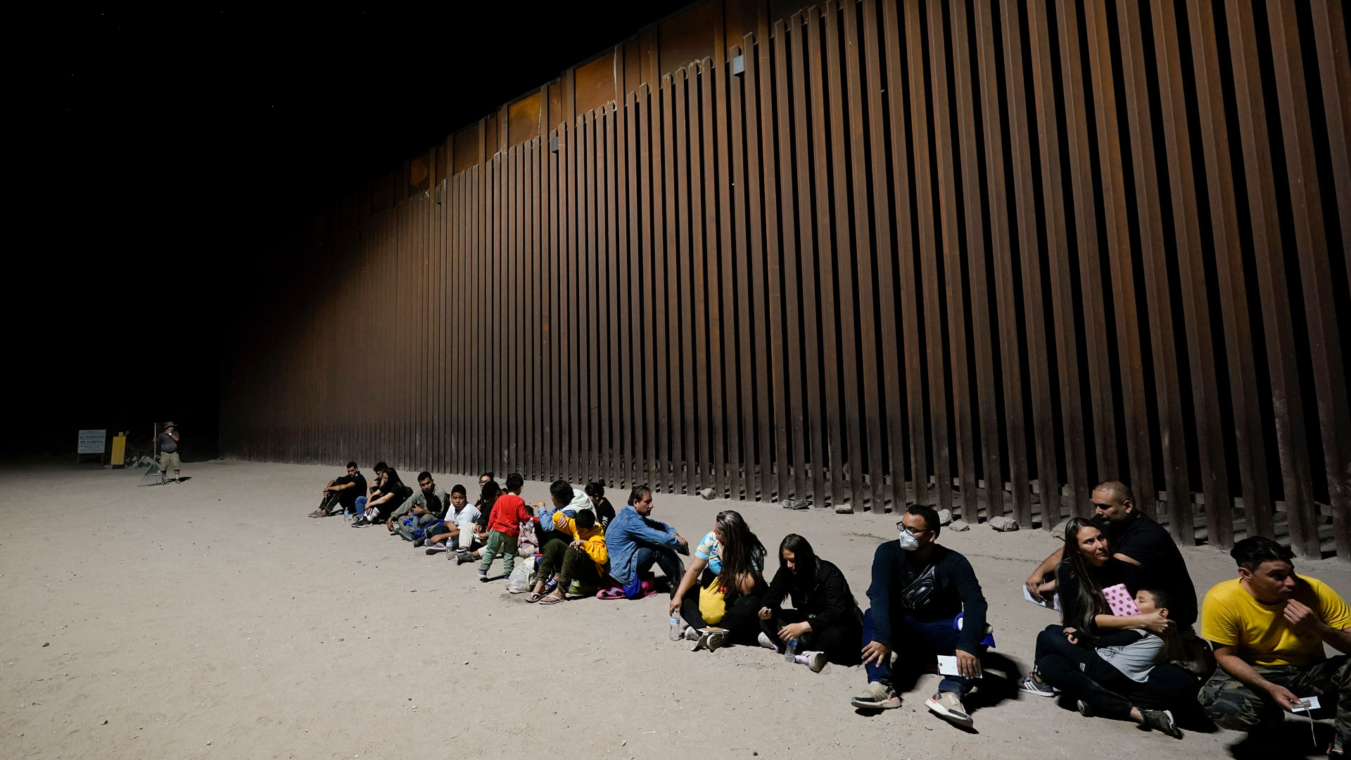 Migrants wait near the end of a border wall Tuesday, Aug. 23, 2022, near Yuma, Ariz.
