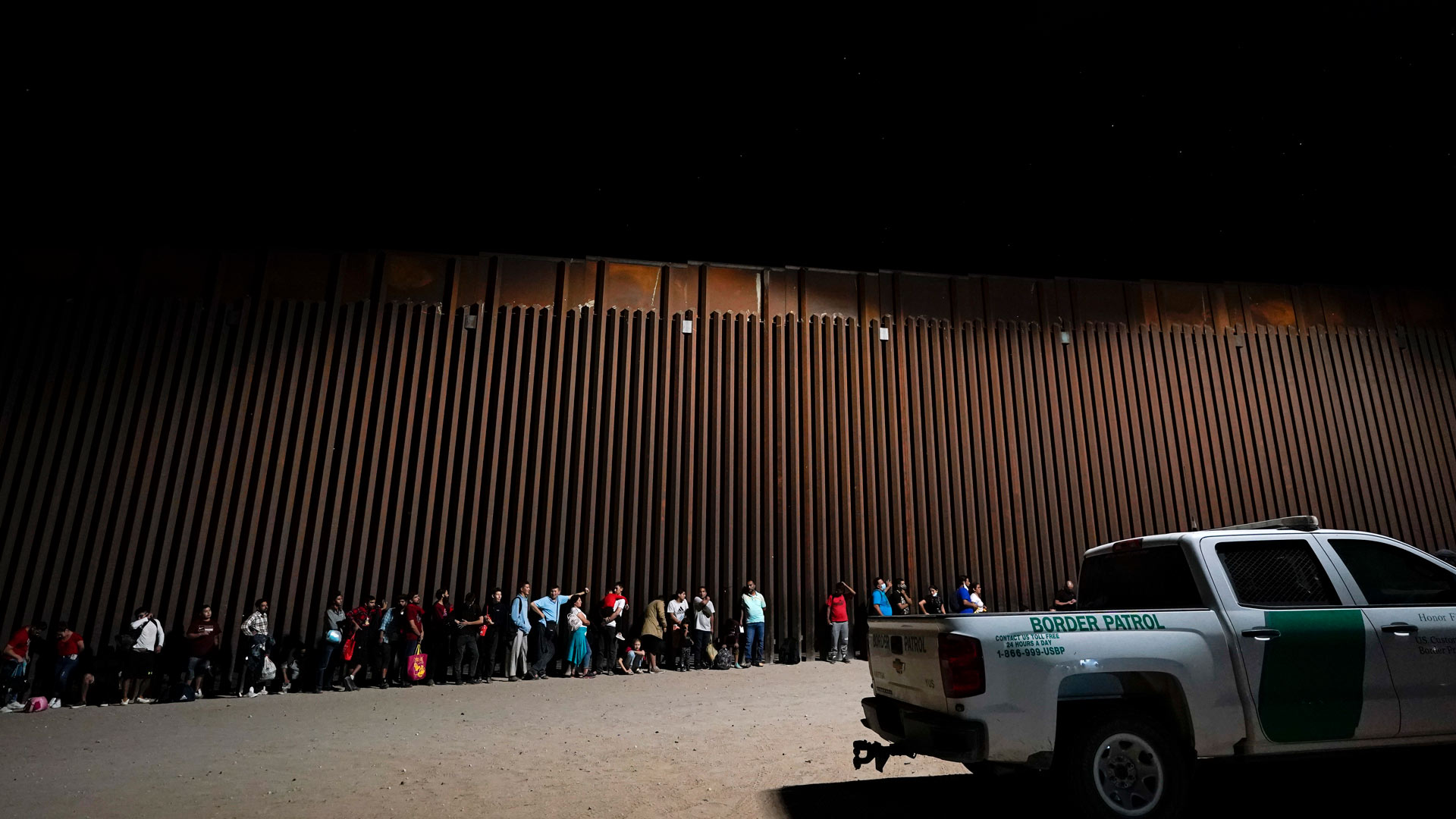 Migrants wait to be processed after crossing into the United States near the end of a border wall Tuesday, Aug. 23, 2022, near Yuma, Ariz. 