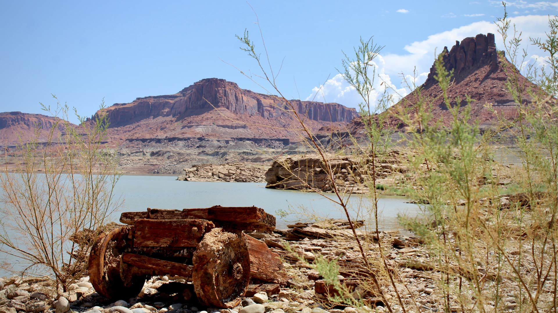 An ore cart, encrusted in invasive mussel shells, rests on a ledge above a receding Lake Powell.