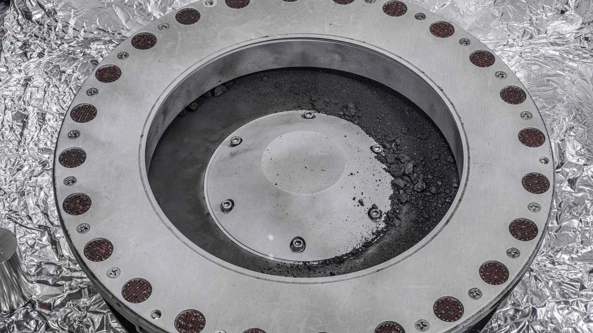 A view of the outside of the OSIRIS-REx sample collector. Sample material from asteroid Bennu can be seen on the middle right. Scientists have found evidence of both carbon and water in initial analysis of this material. The bulk of the sample is located inside.