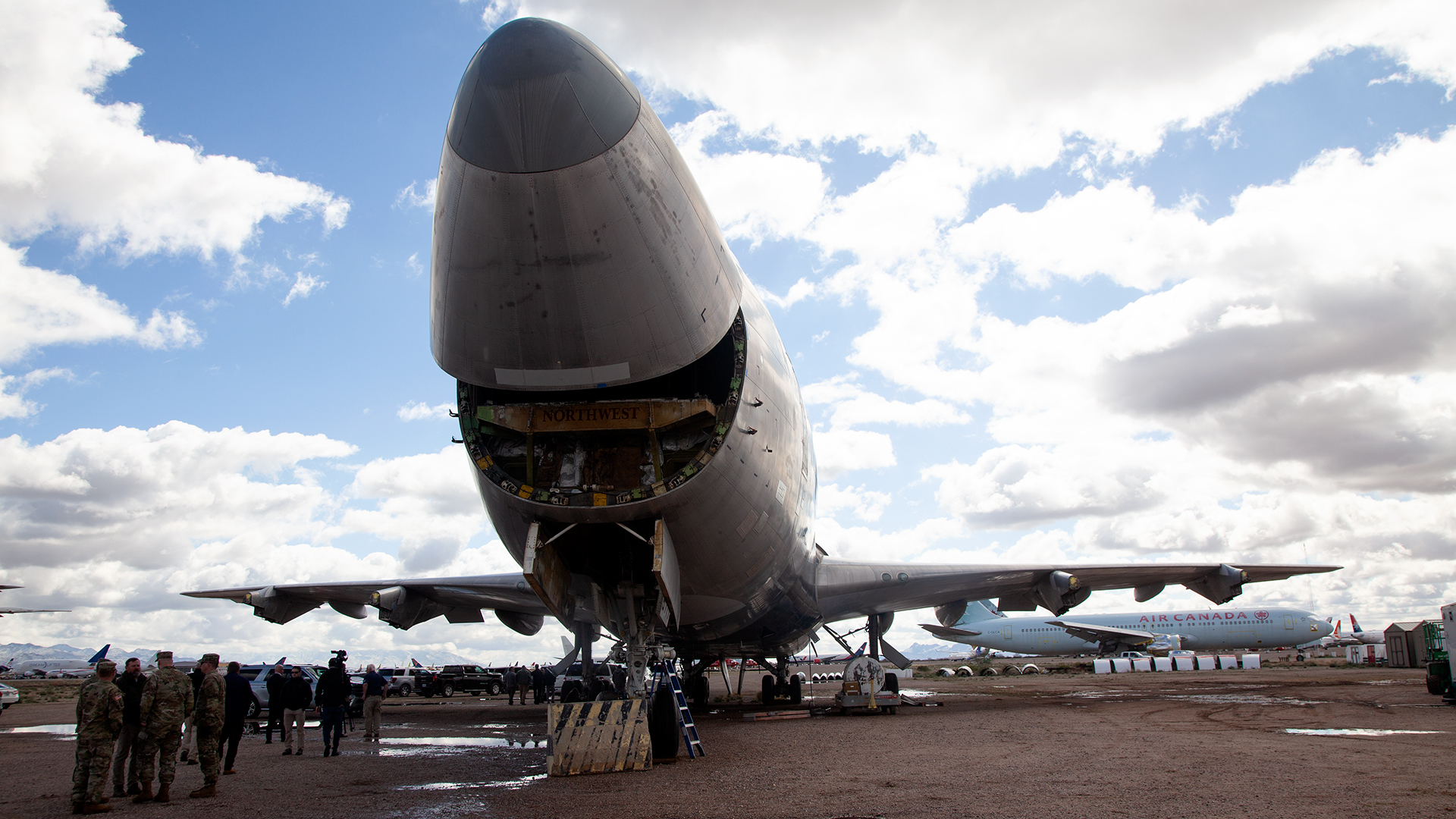 A group of military members gather under a decommissioned aircraft