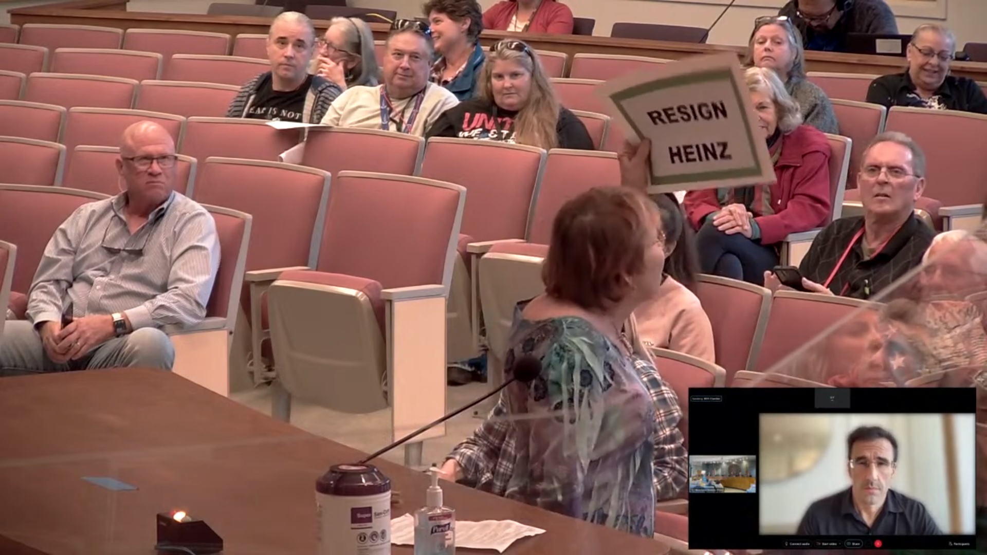 Shirley Requard displays a "Resign Heinz" sign at a Pima County Board of Supervisors meeting on February 21, 2023, as supervisor Matt Heinz watches (lower right).