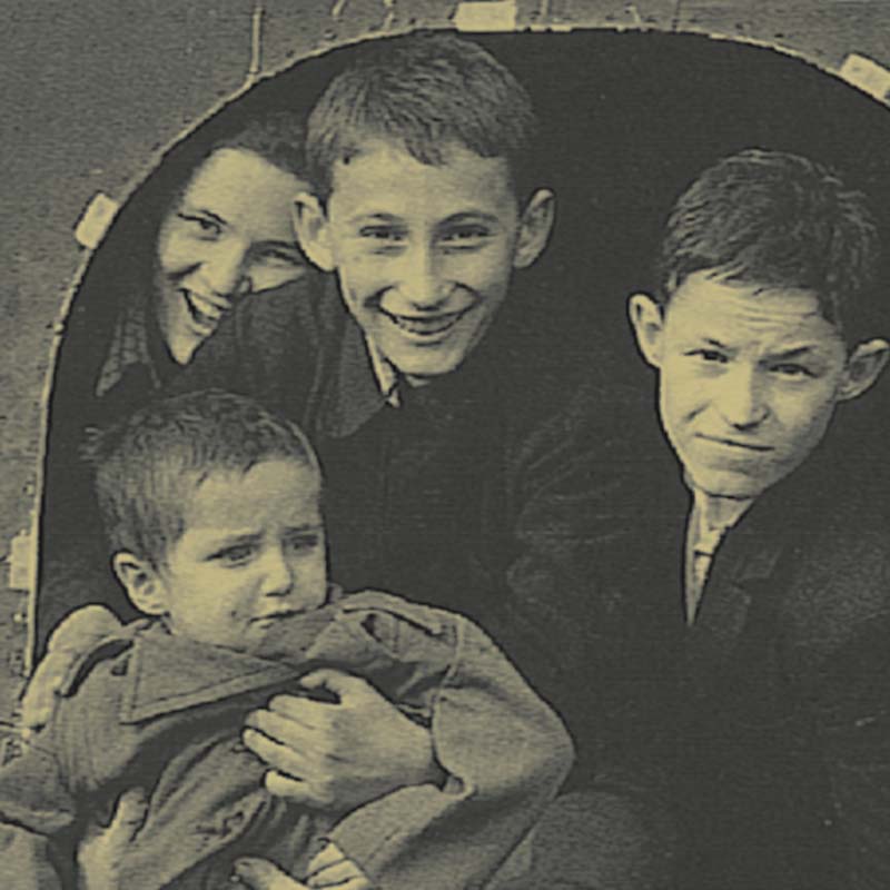 Sidney (center top, smiling), on the transport plane that brought him to England. His brother, Isaac (left), is helping a two-year-old orphan.