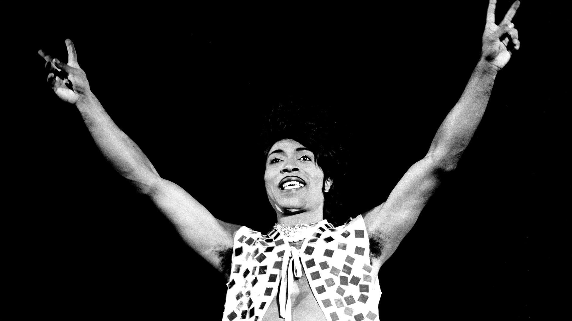 LITTLE RICHARD - US rock musician arms in air doing peace sign in glitter vest.