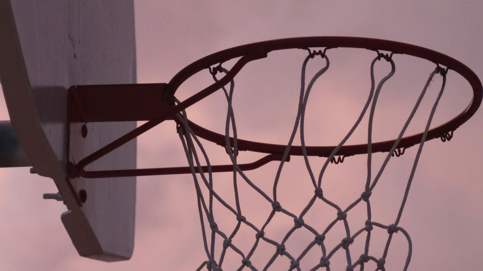 A basketball hoop is silhouetted against the sunset.
