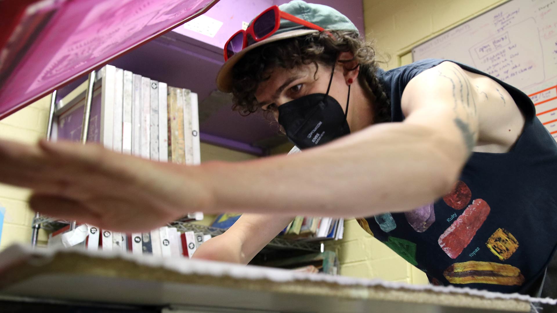 Alyx Lunada lays a piece of cloth on the printing press at Word of Mouth Print Space on June 22. They have been screen printing since age 17 and have opened up this space for art and activism to the community.