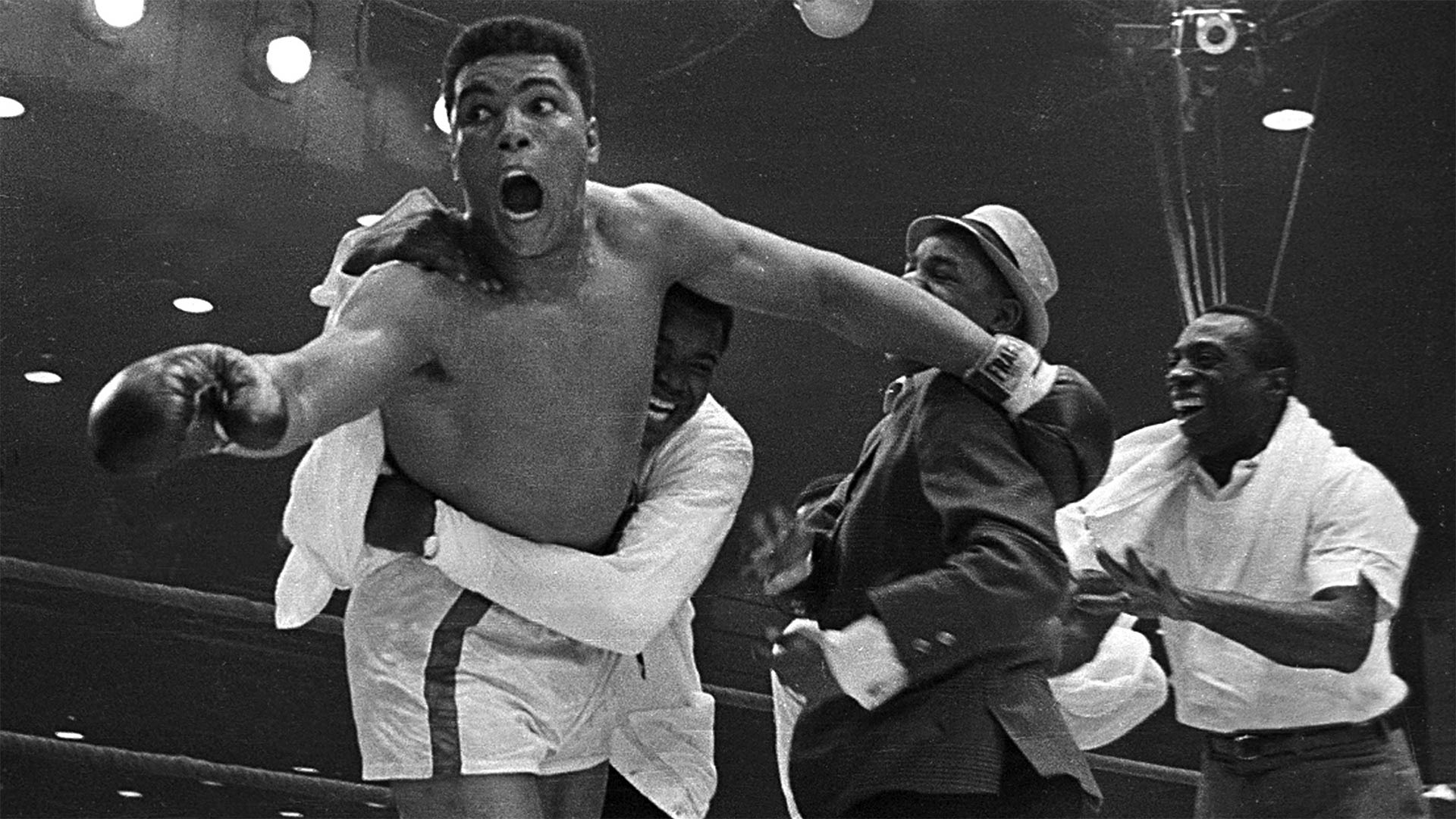 Cassius Clay's handlers hold him back after he is announced the new heavyweight champion of the world after knocking out Sonny Liston. Bundini Brown embraces Ali. Luis Sarria runs to the group in a smile on the right. Miami, Florida. February 25, 1965.
